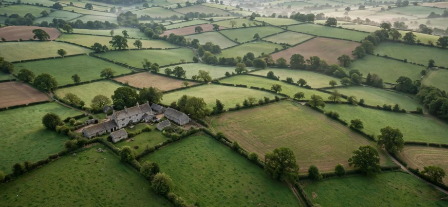 Aerial view of rolling green English farmland with hedgerows and a stone farmhouse